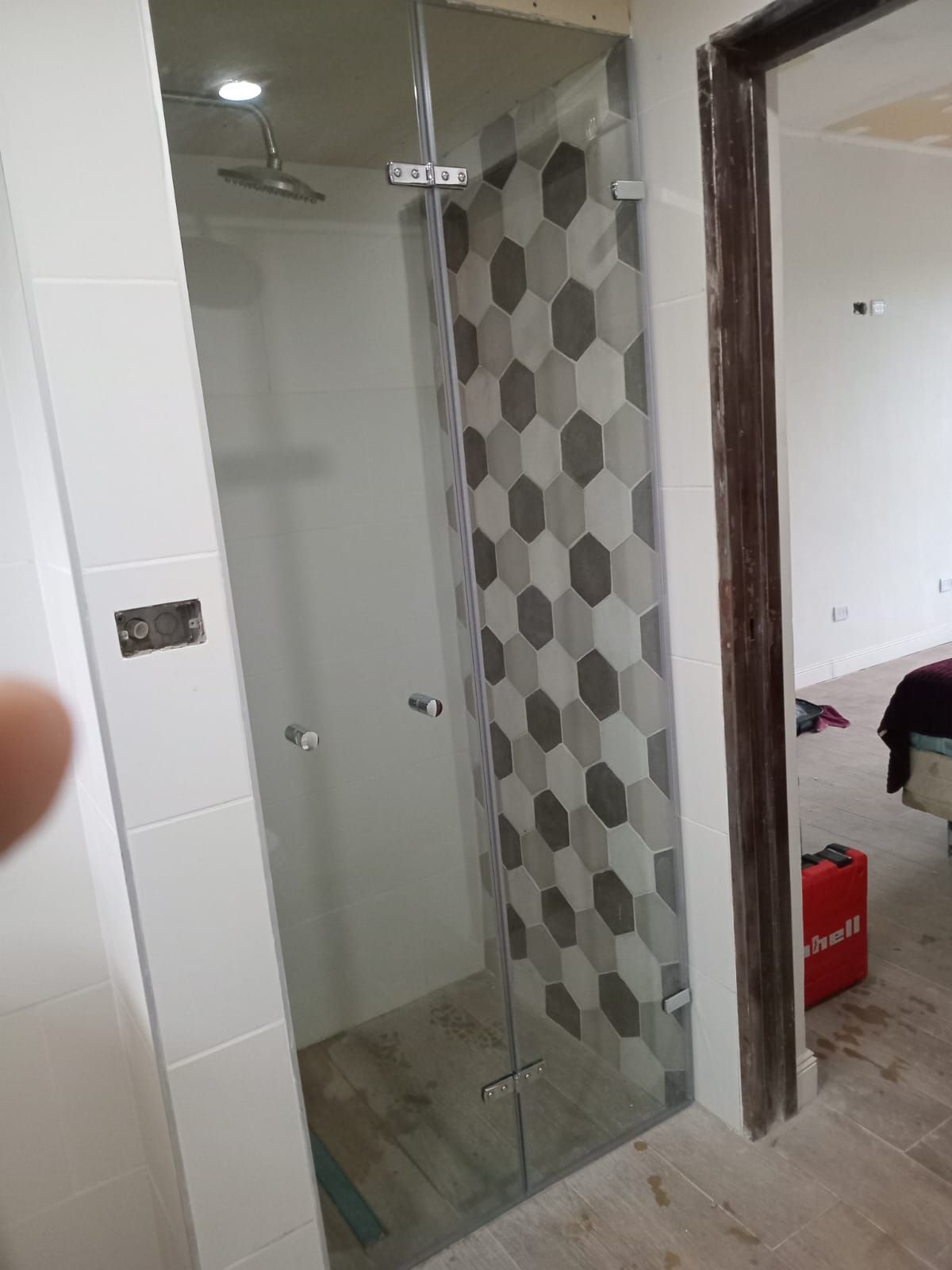 Mampara de ducha de cristal con reverso de baldosas hexagonales de color gris, blanco y negro.