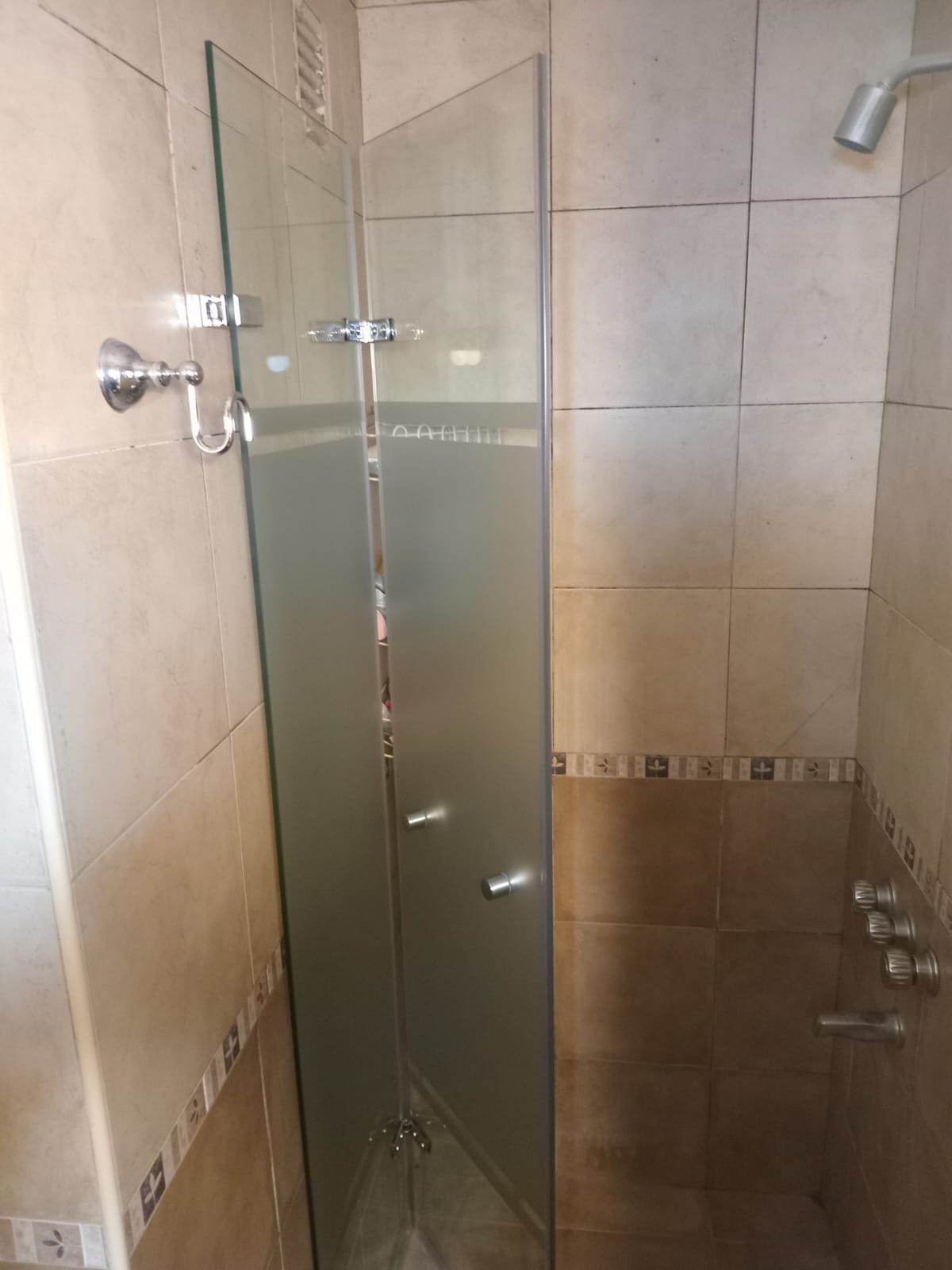 Cabina de ducha con puertas de vidrio, herrajes plateados y paredes de azulejos beige.