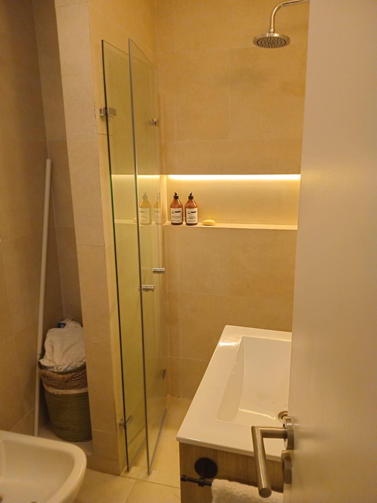 Baño con ducha de cristal, bañera y combinación de colores neutros.