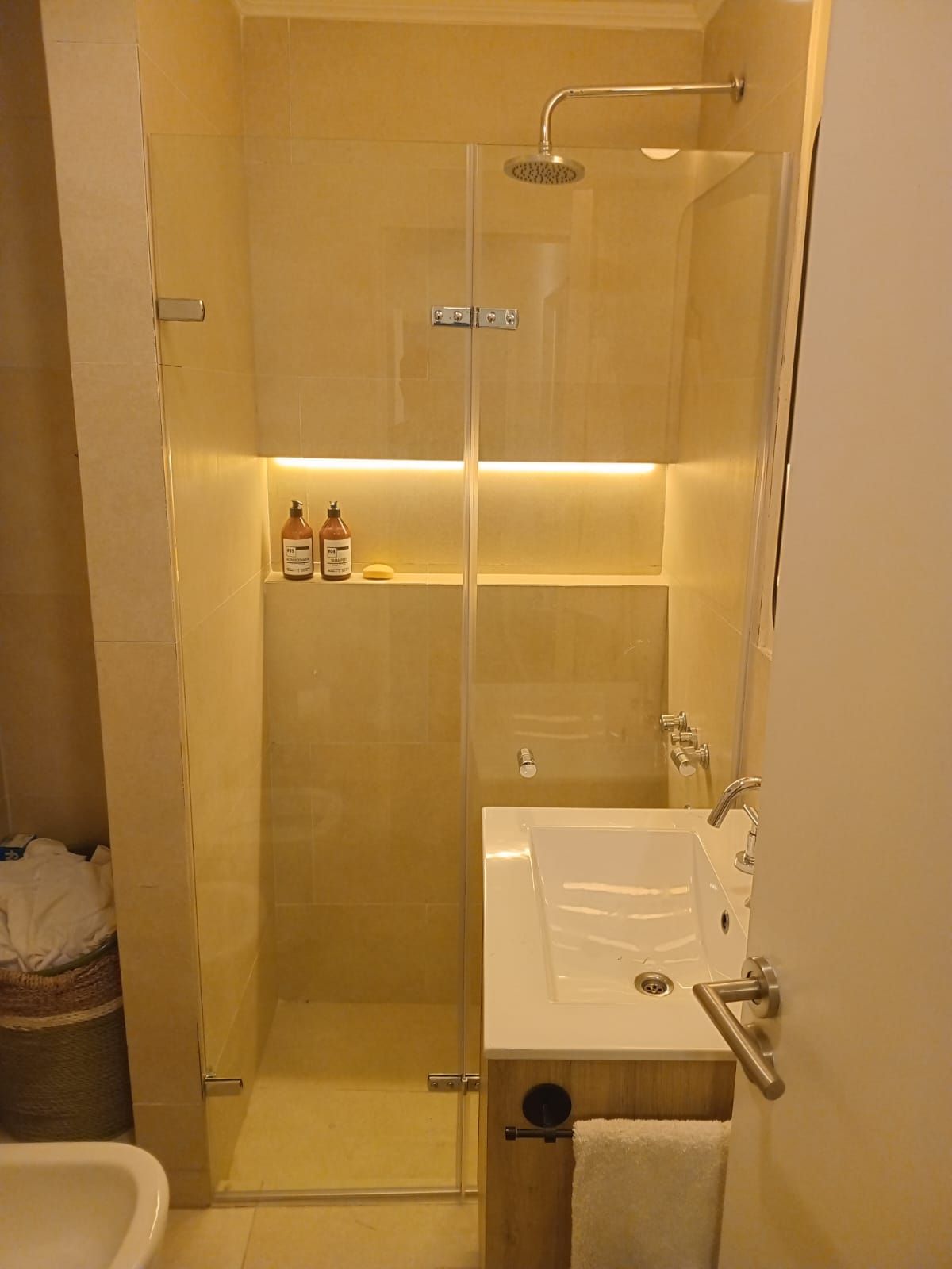 Un baño pequeño con ducha con mampara de cristal, estantes empotrados y lavabo.