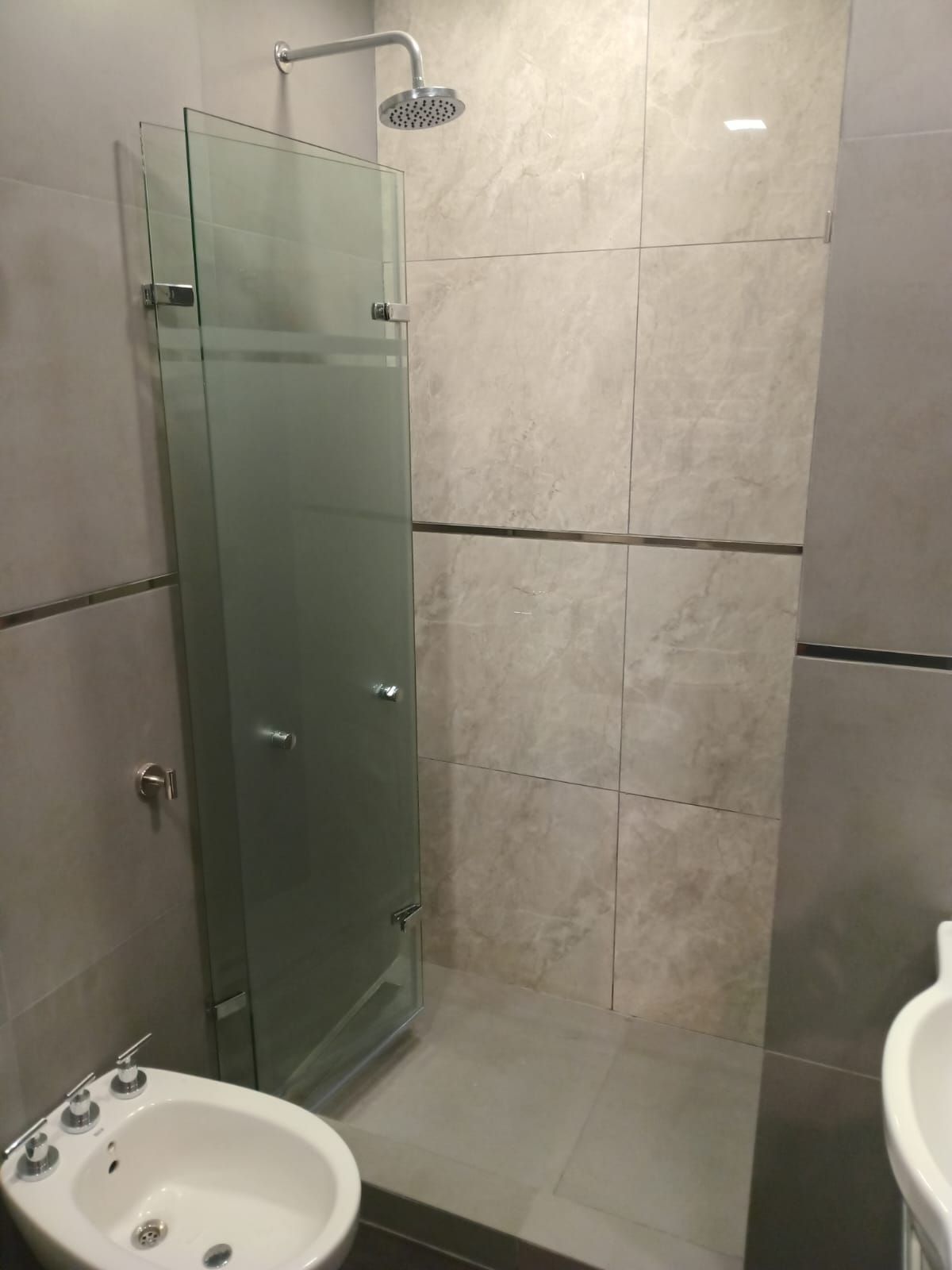 Mampara de ducha con puerta de cristal esmerilado, bidé y paredes alicatadas en un baño moderno.