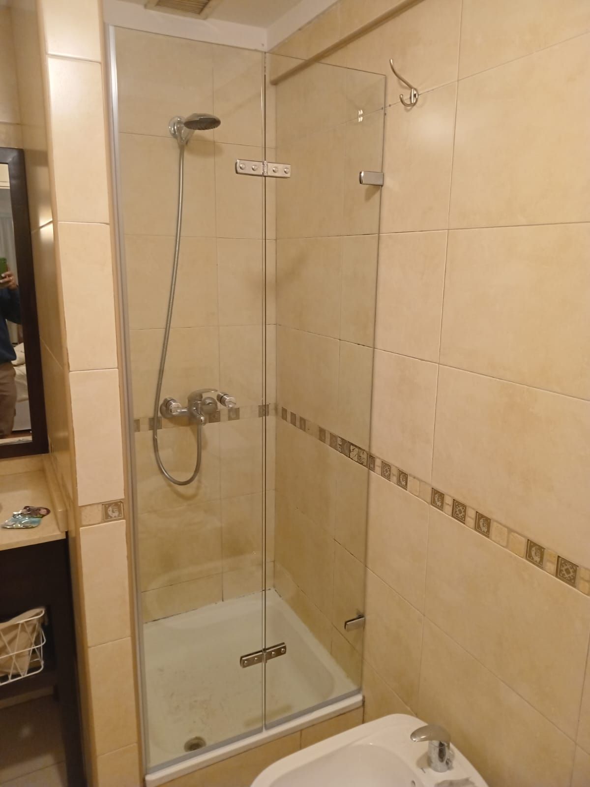 Cabina de ducha con puerta de cristal, accesorios plateados y azulejos beige en un baño.