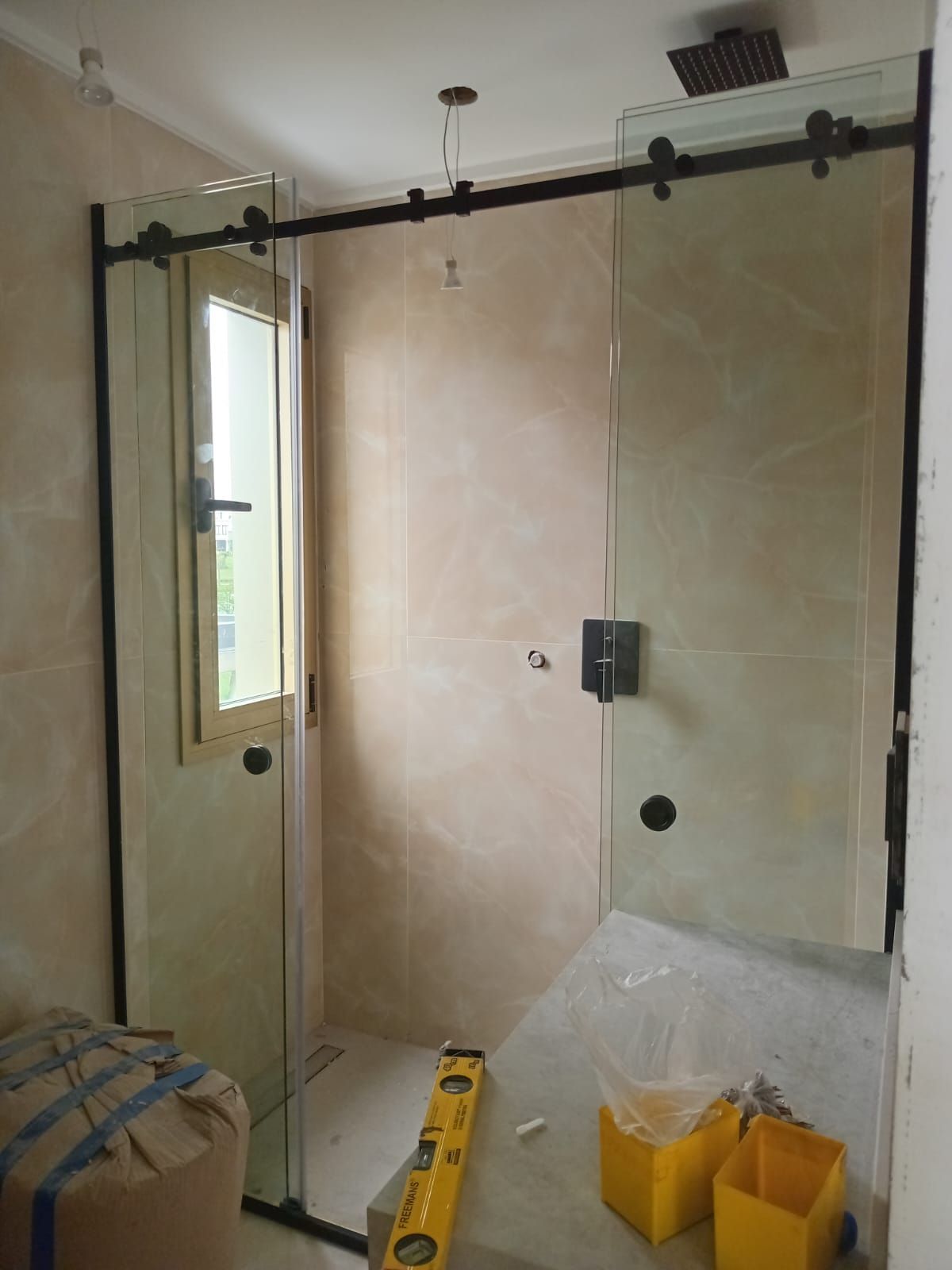 Mampara de ducha de cristal con marco negro y puerta corredera, en construcción. Las paredes interiores están alicatadas