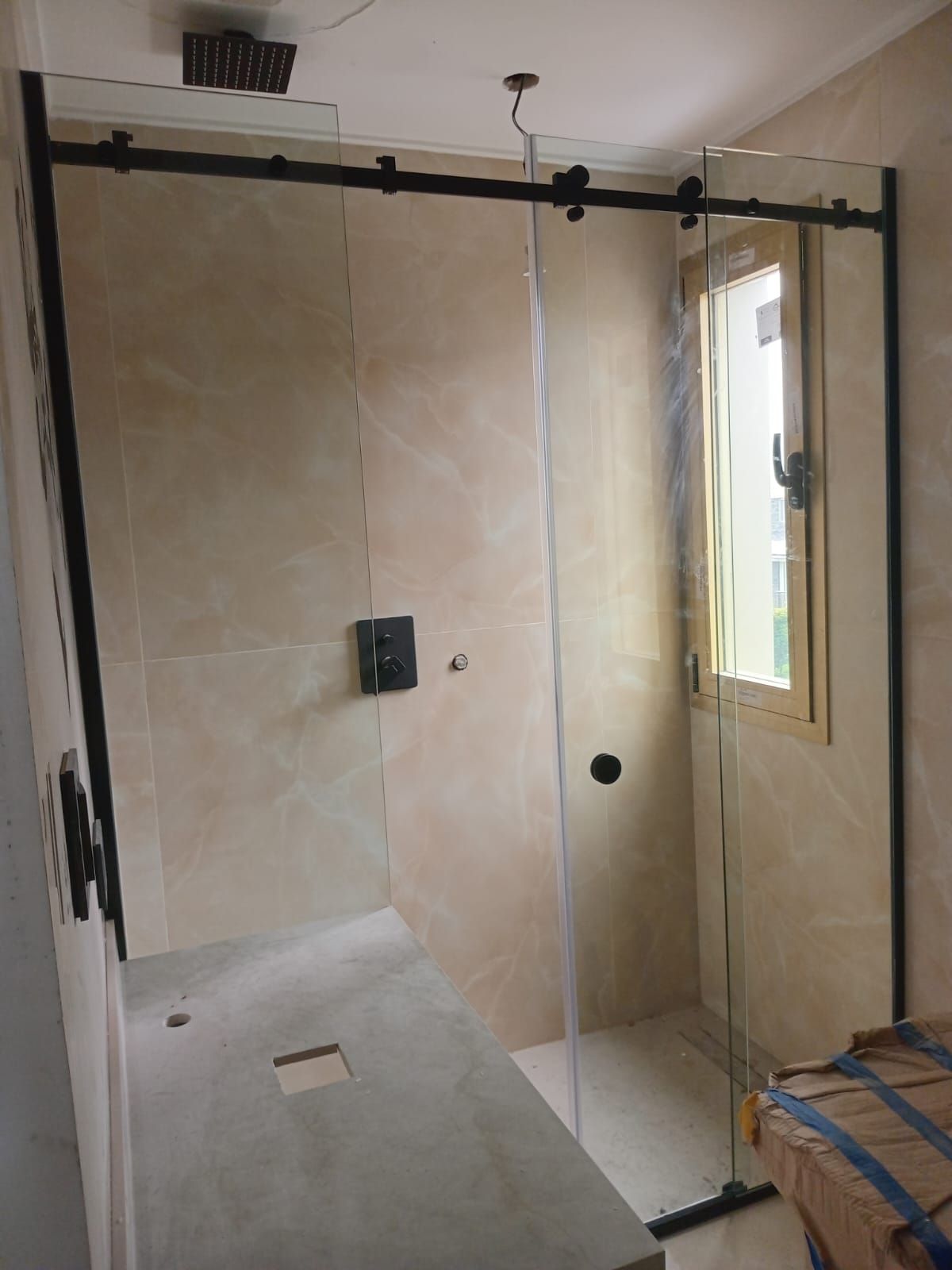 Mampara de ducha con marco negro, puertas de cristal y paredes alicatadas; incluye ventana.