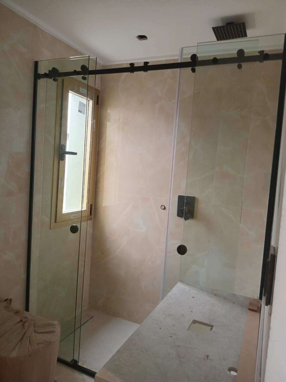 Mampara de ducha de cristal con estructura de metal negro y puerta corredera, paredes de azulejos beige.