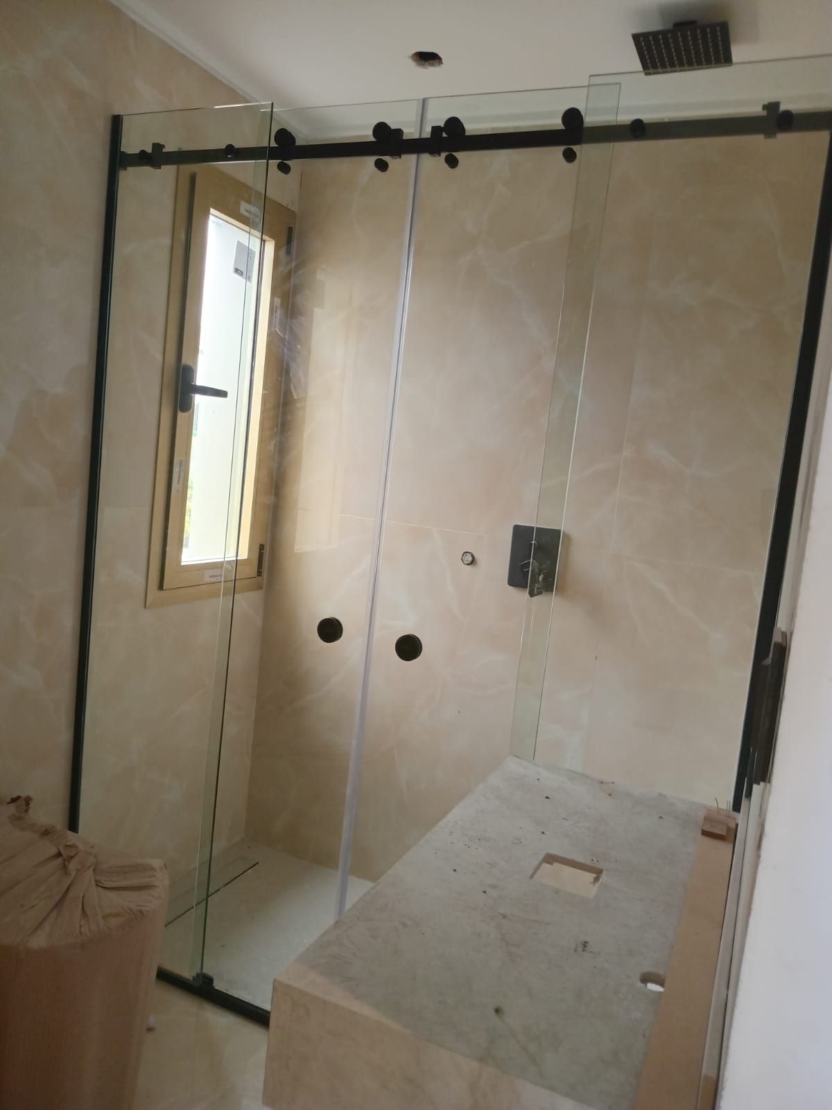 Mampara de ducha con puertas correderas de cristal, marco negro y paredes revestidas de azulejos beige.