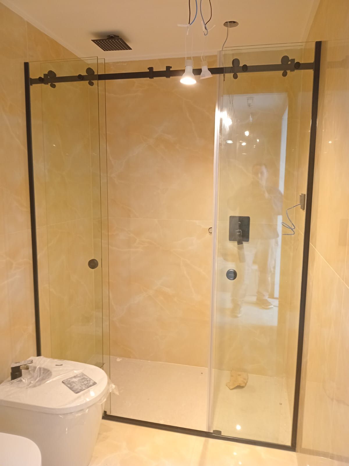 Baño con mampara de ducha de cristal con marco negro. Paredes de color amarillo pálido.