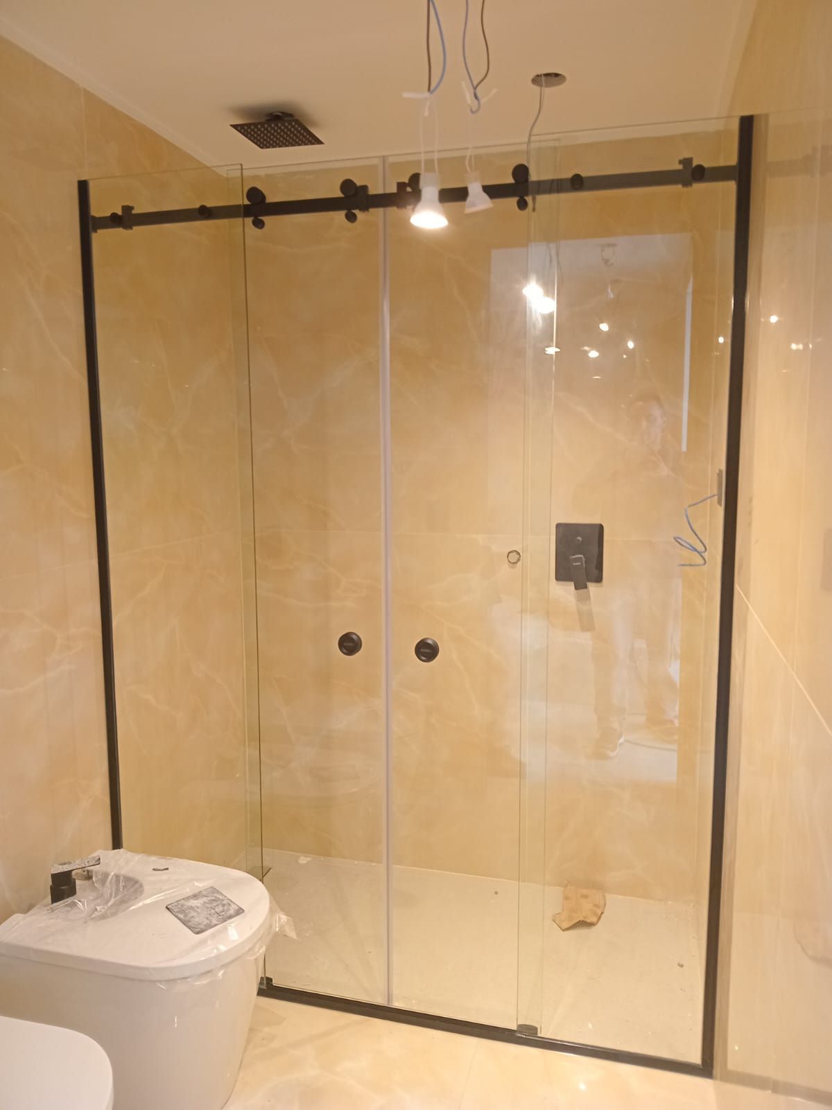 Mampara de ducha de cristal con estructura y herrajes de metal negro, en un baño con azulejos de color beige.