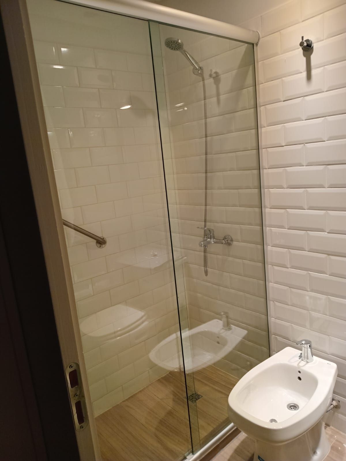 Baño con ducha de cristal, paredes de azulejos blancos tipo metro y bidé.