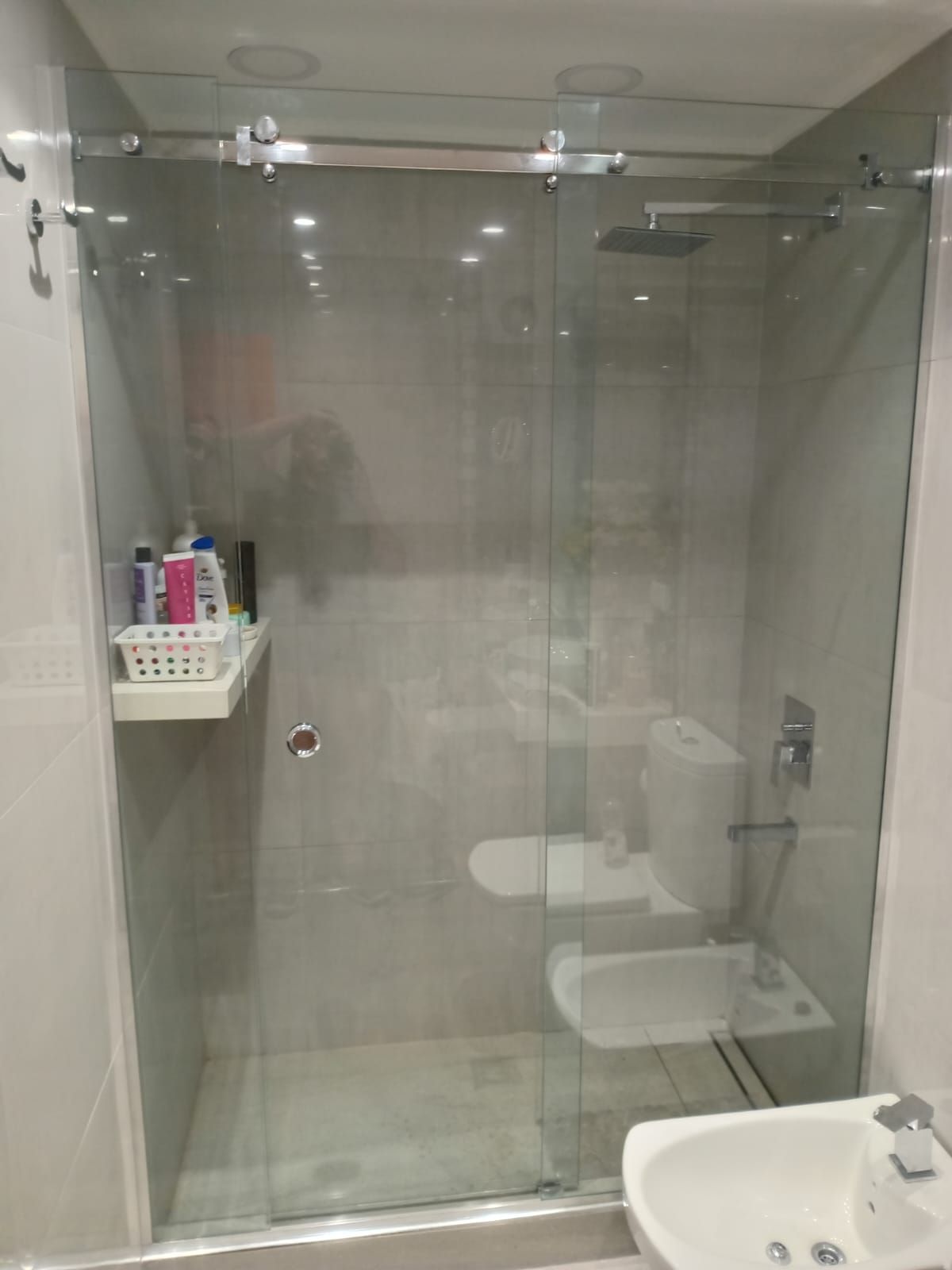 Cabina de ducha con puertas corredizas de vidrio, inodoro y lavabo en un baño moderno.