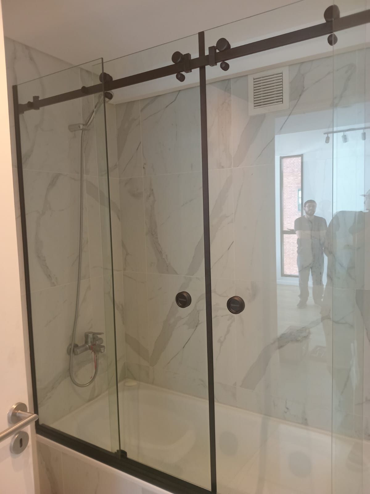 Puertas de ducha corredizas de vidrio con marco de metal negro sobre una bañera blanca.