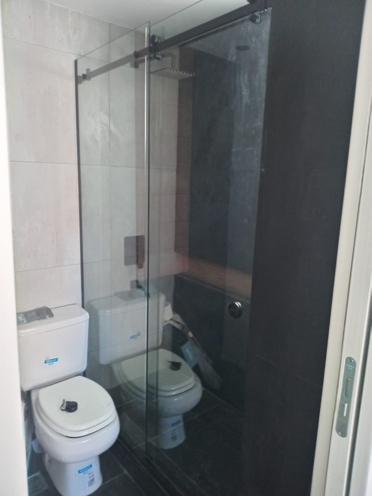 Baño con mampara de ducha de cristal y dos aseos.