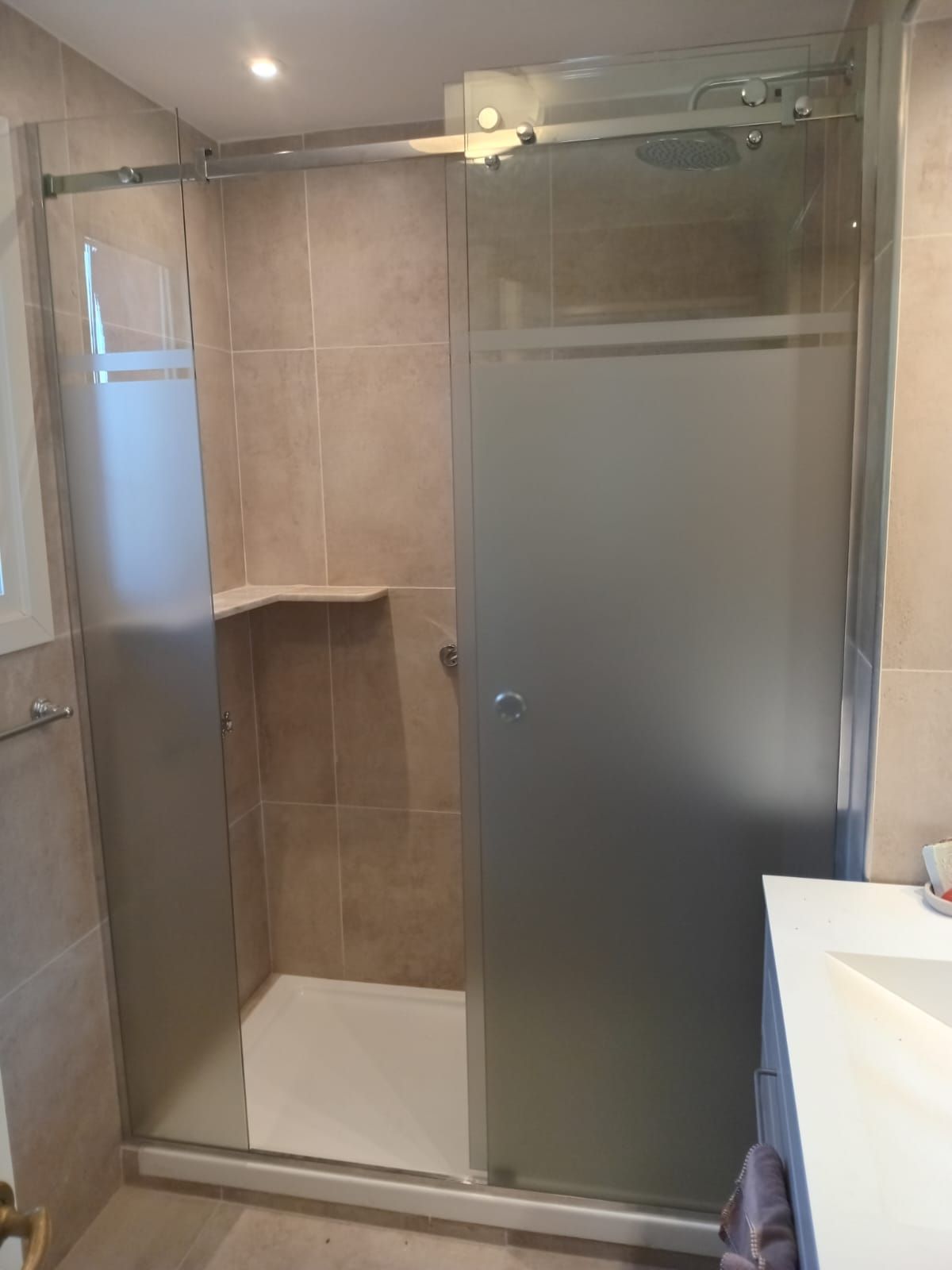 Mampara de ducha con puerta de cristal esmerilado y paredes de azulejos beige.