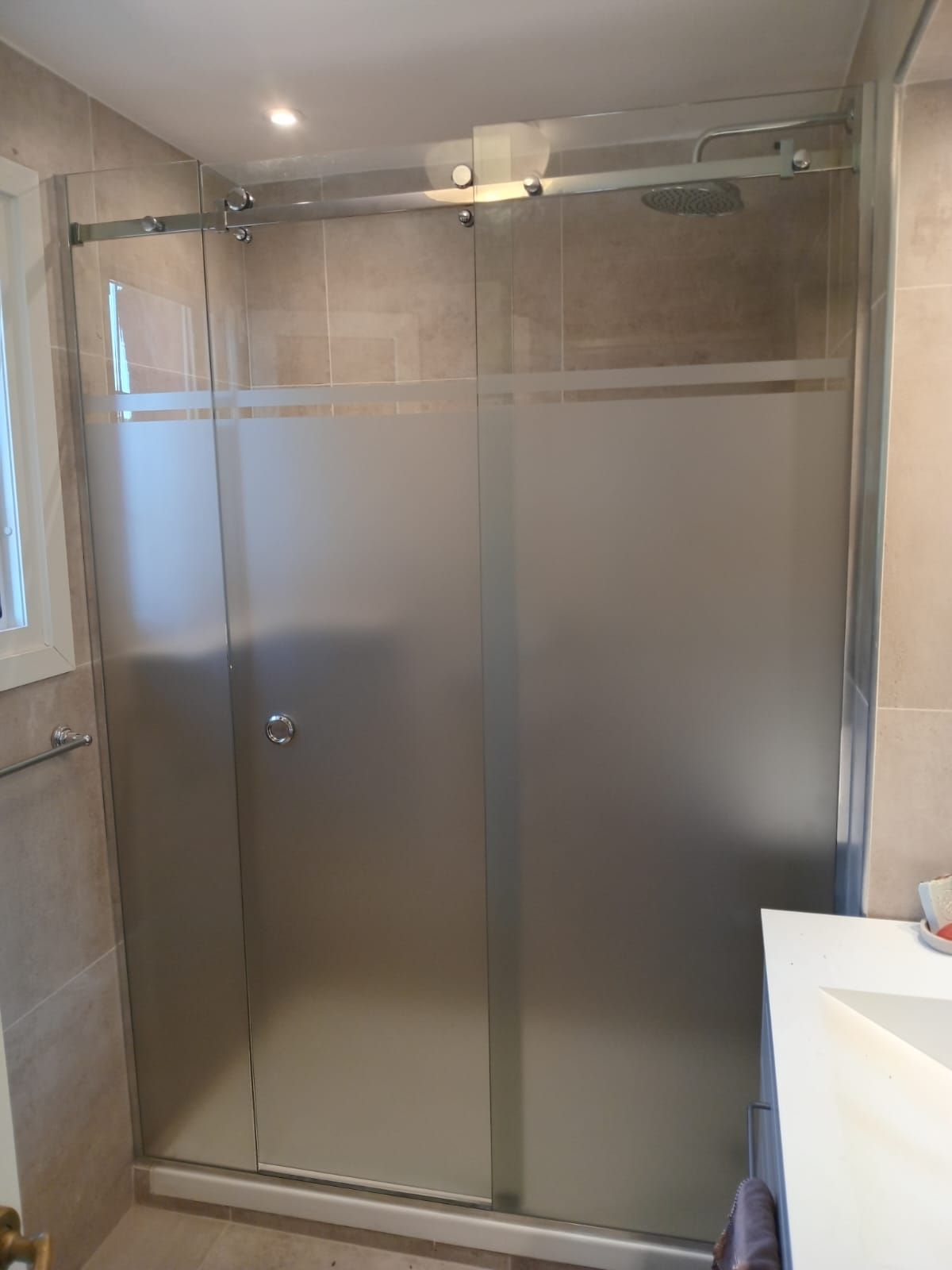 Ducha con puertas de vidrio esmerilado en un baño con paredes de azulejos color canela.