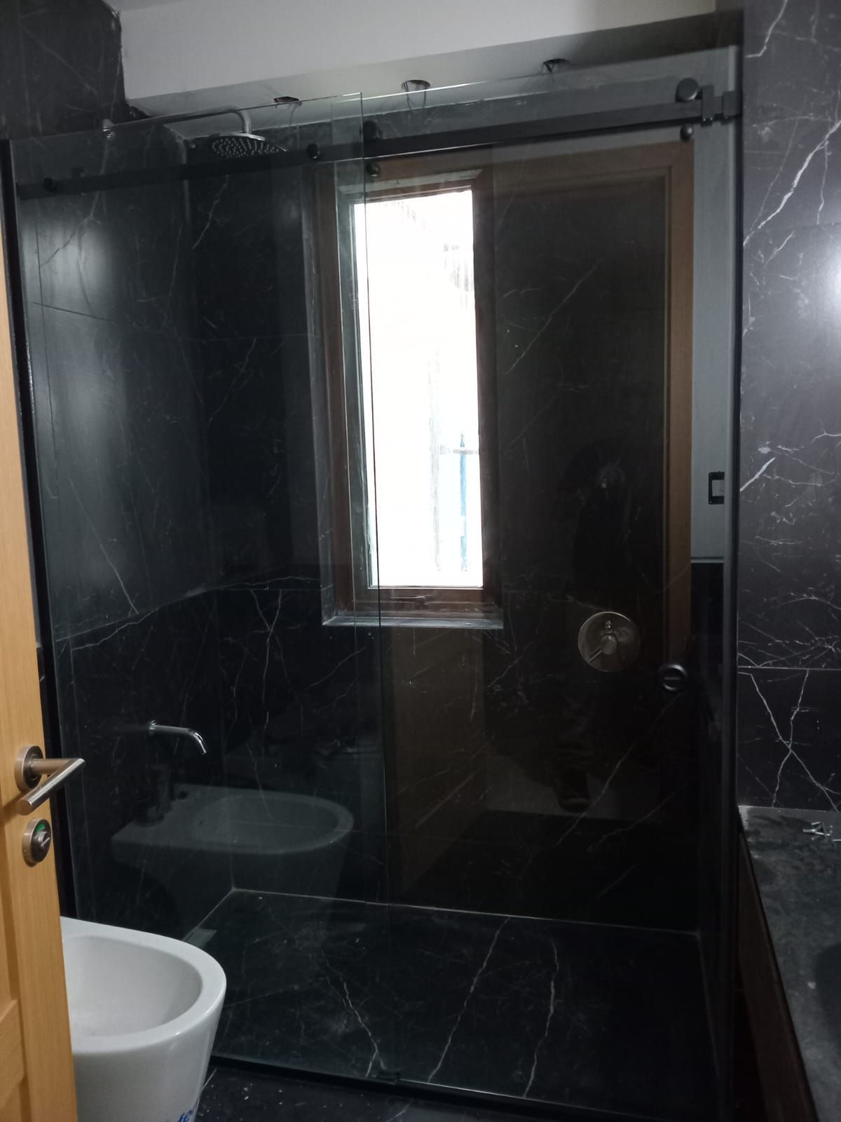 Baño de mármol negro con ducha de cristal, inodoro y ventana.