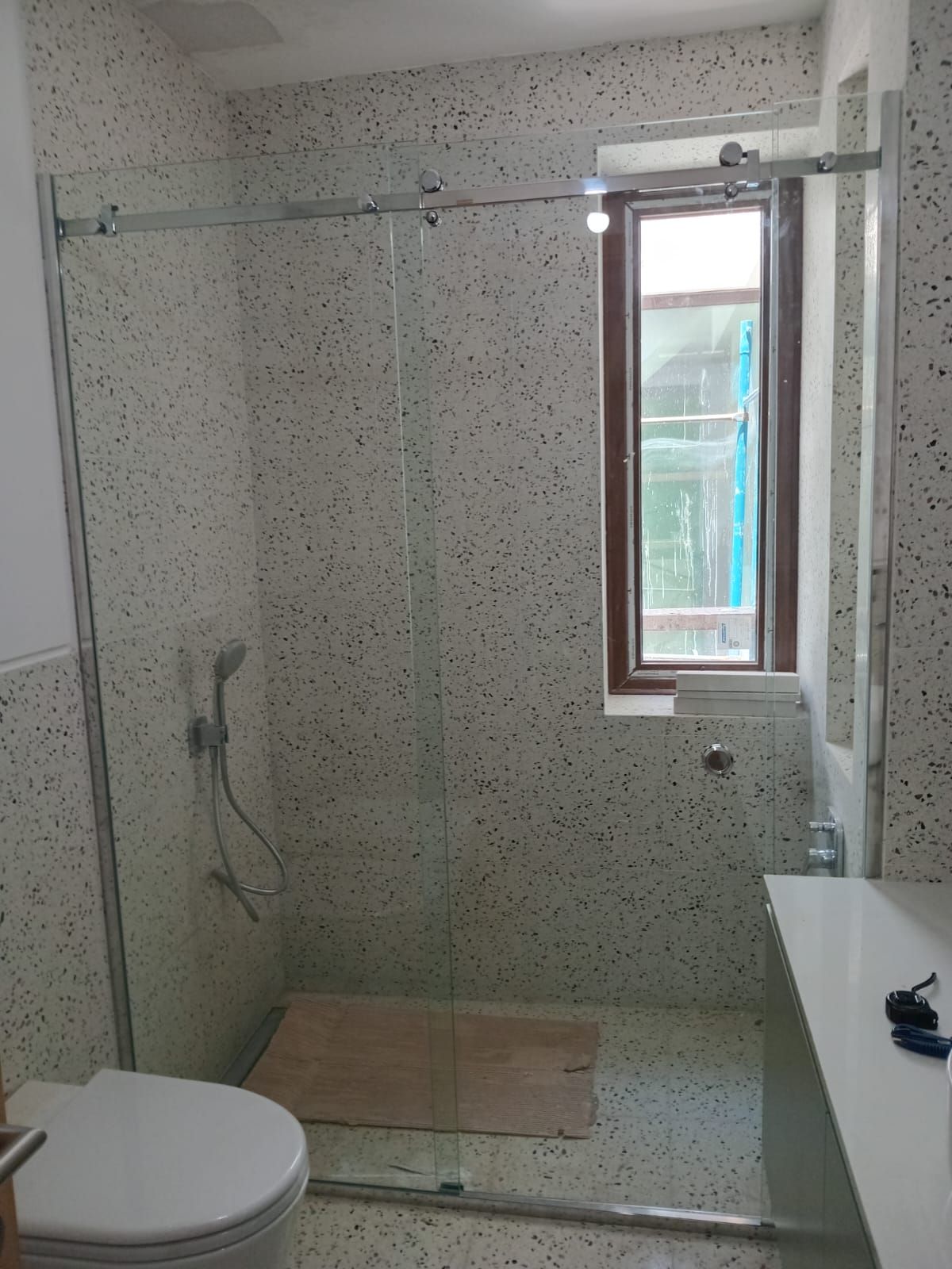 Baño con puerta de ducha de cristal, paredes moteadas, inodoro, ventana.