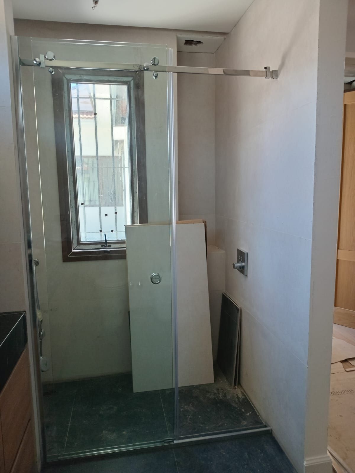 Cabina de ducha con puerta de cristal y barra metálica. Ventana tras cristal. Suelo de tablas.