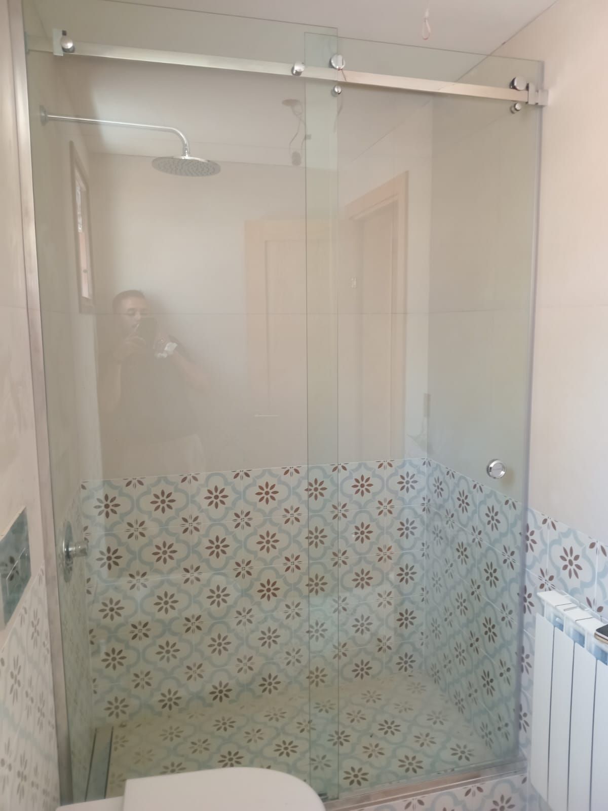 Ducha con puerta corredera de cristal y azulejos estampados.