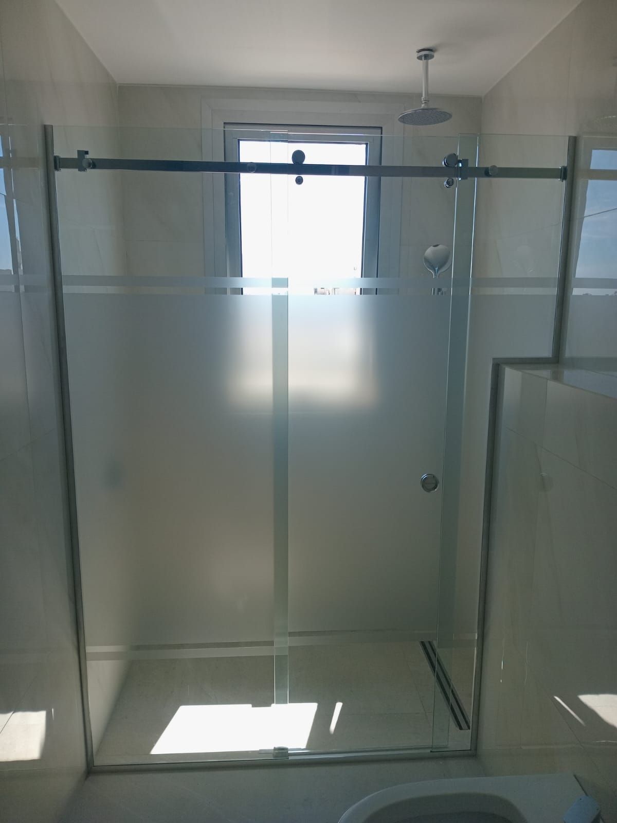 Mampara de ducha con paneles de cristal esmerilado, ventana en la pared trasera y cabezal de ducha.