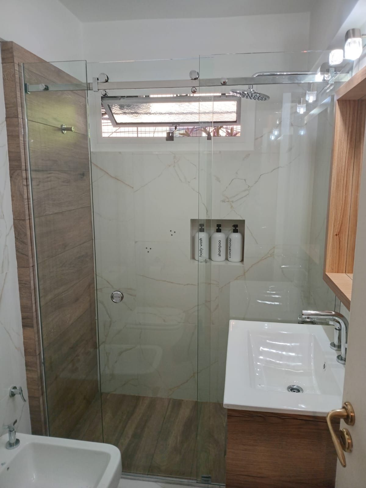 Baño moderno con mampara de ducha de cristal, tocador y combinación de colores neutros.
