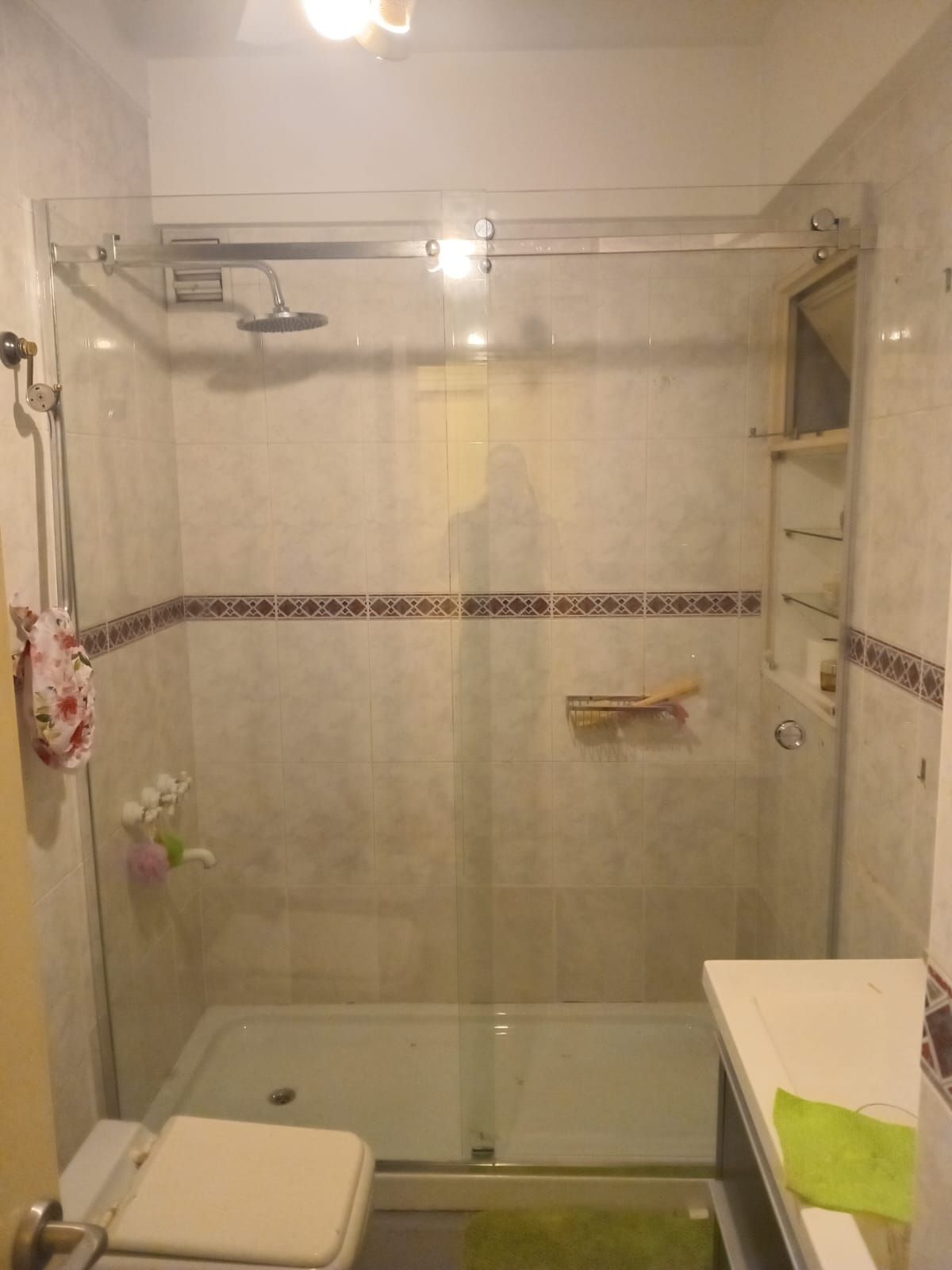 Cabina de ducha con puertas de cristal, paredes de azulejos y cabezal de ducha.