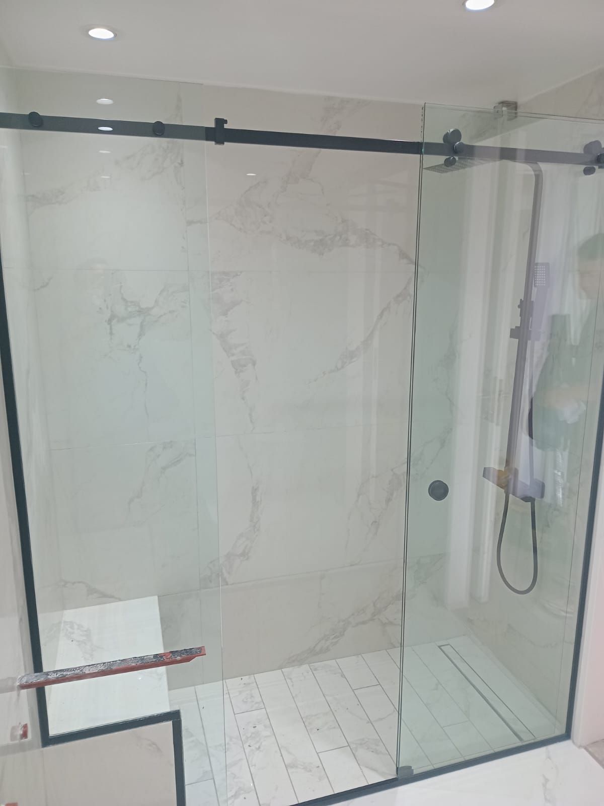 Mampara de ducha de cristal con marco negro y puerta corredera en baño con azulejos efecto mármol.