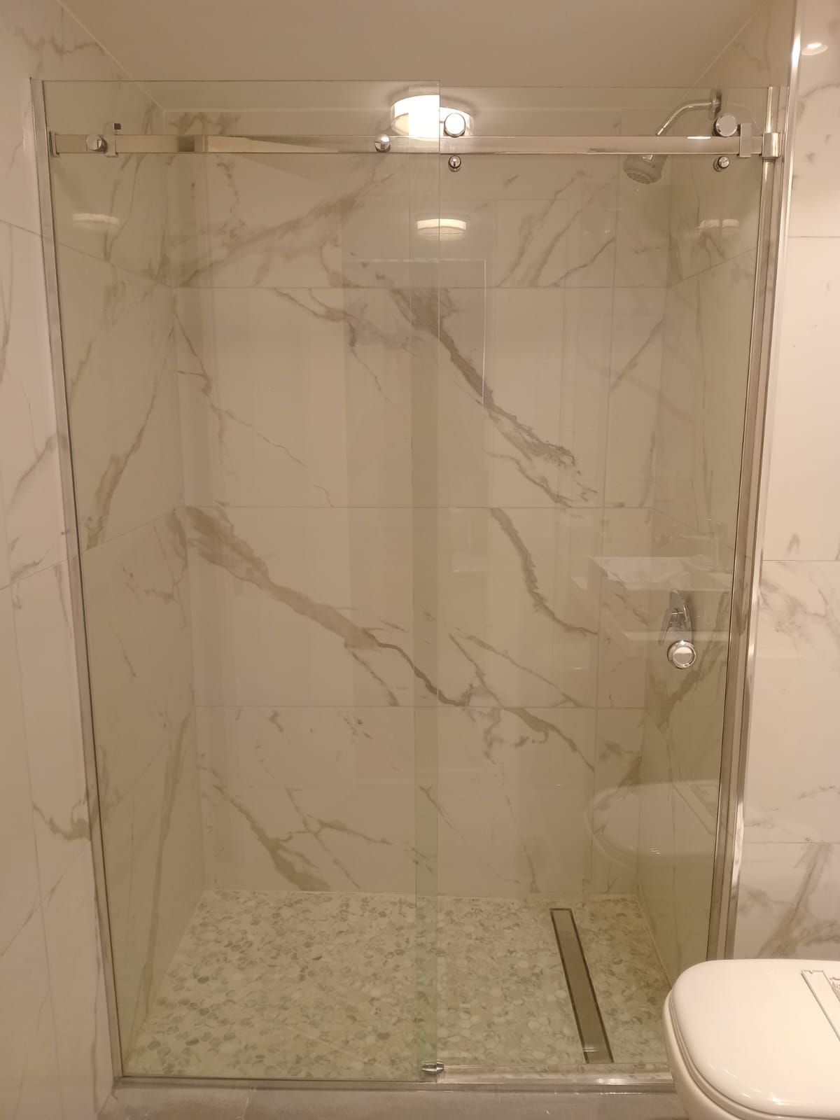 Ducha de cristal con paredes y suelo con estampado de mármol, puerta corrediza y accesorios cromados.