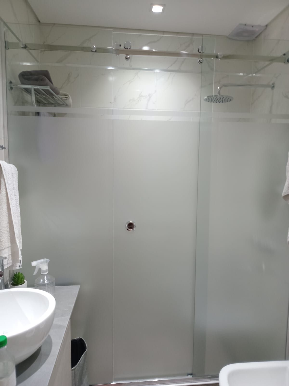 Baño con mampara de ducha de cristal esmerilado, lavabo blanco, toallas y encimera gris.