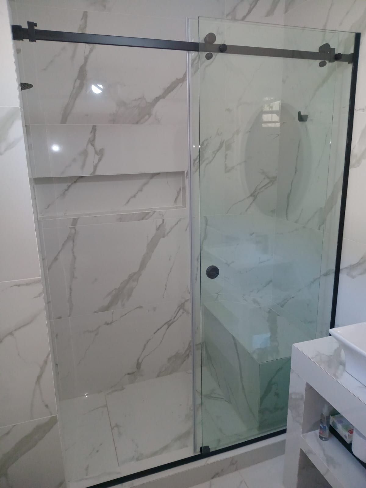 Ducha con puerta corrediza de vidrio y paredes revestidas de mármol, herrajes negros.