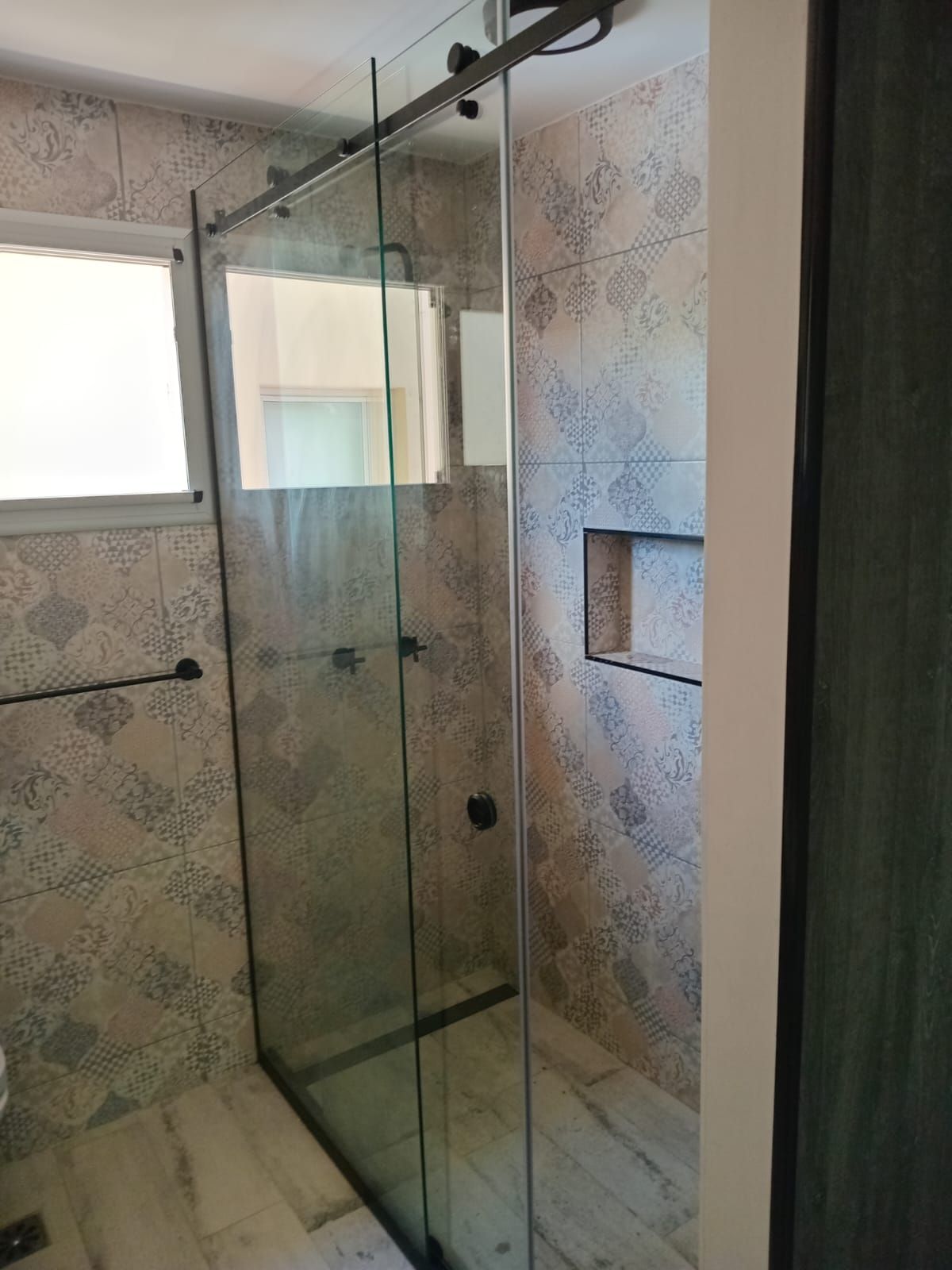 Mampara de ducha de cristal con puerta corredera y azulejo decorativo en baño.