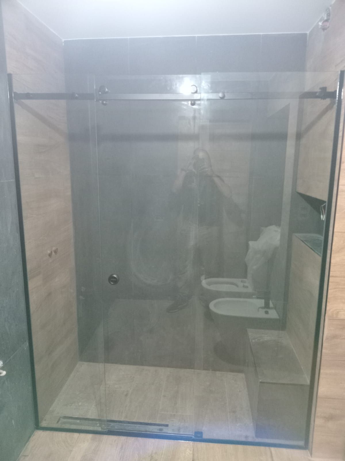 Mampara de ducha de cristal en un baño con inodoro y bidé visibles al fondo.