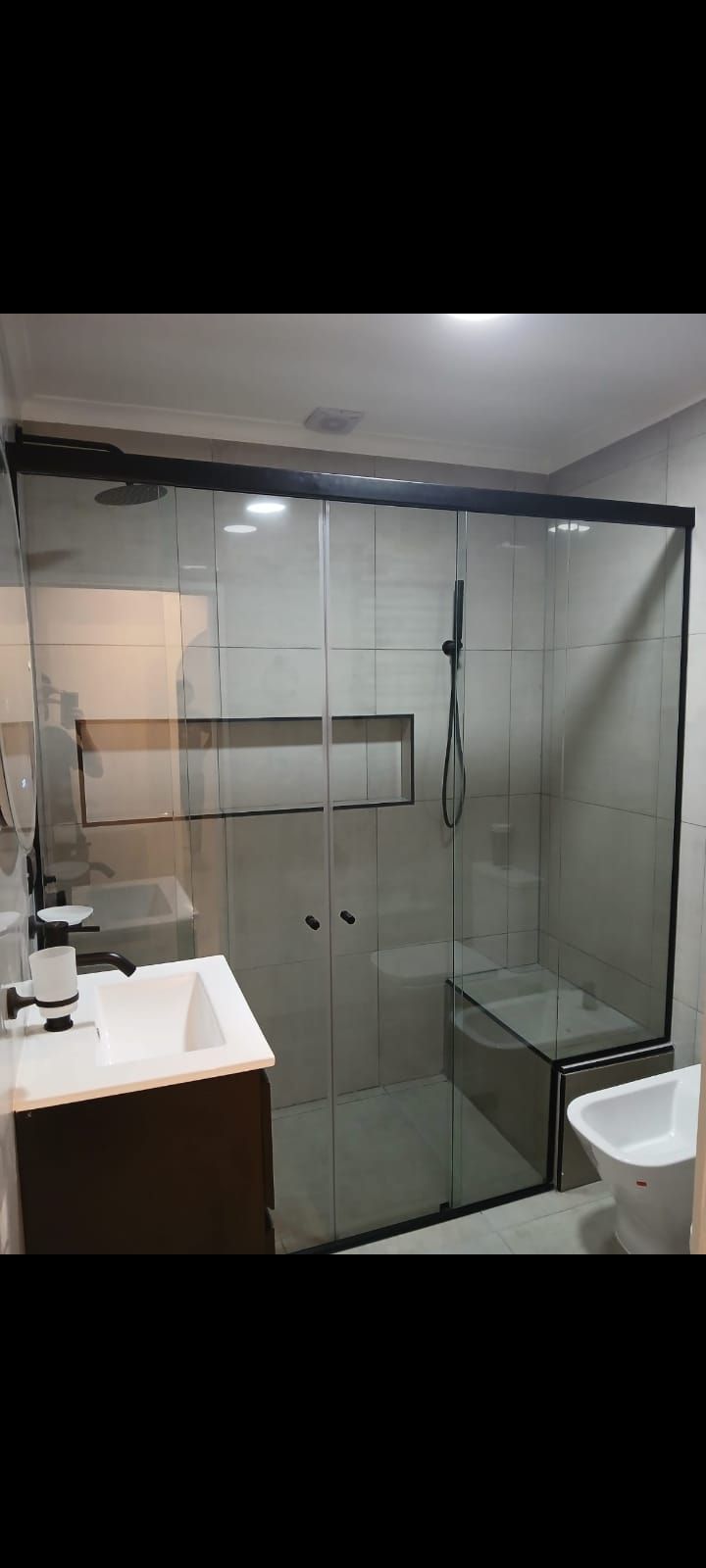 Baño con puertas de ducha de cristal y lavabo blanco.