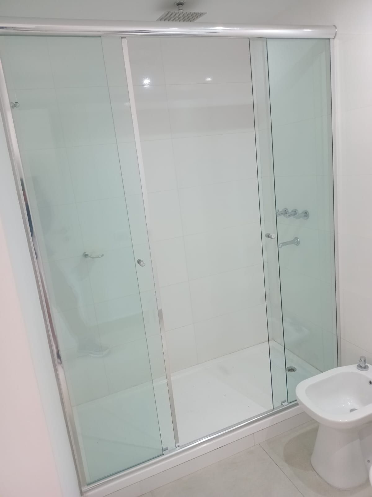 Mampara de ducha con puertas correderas de cristal esmerilado y marco de acero inoxidable. Inodoro en esquina.