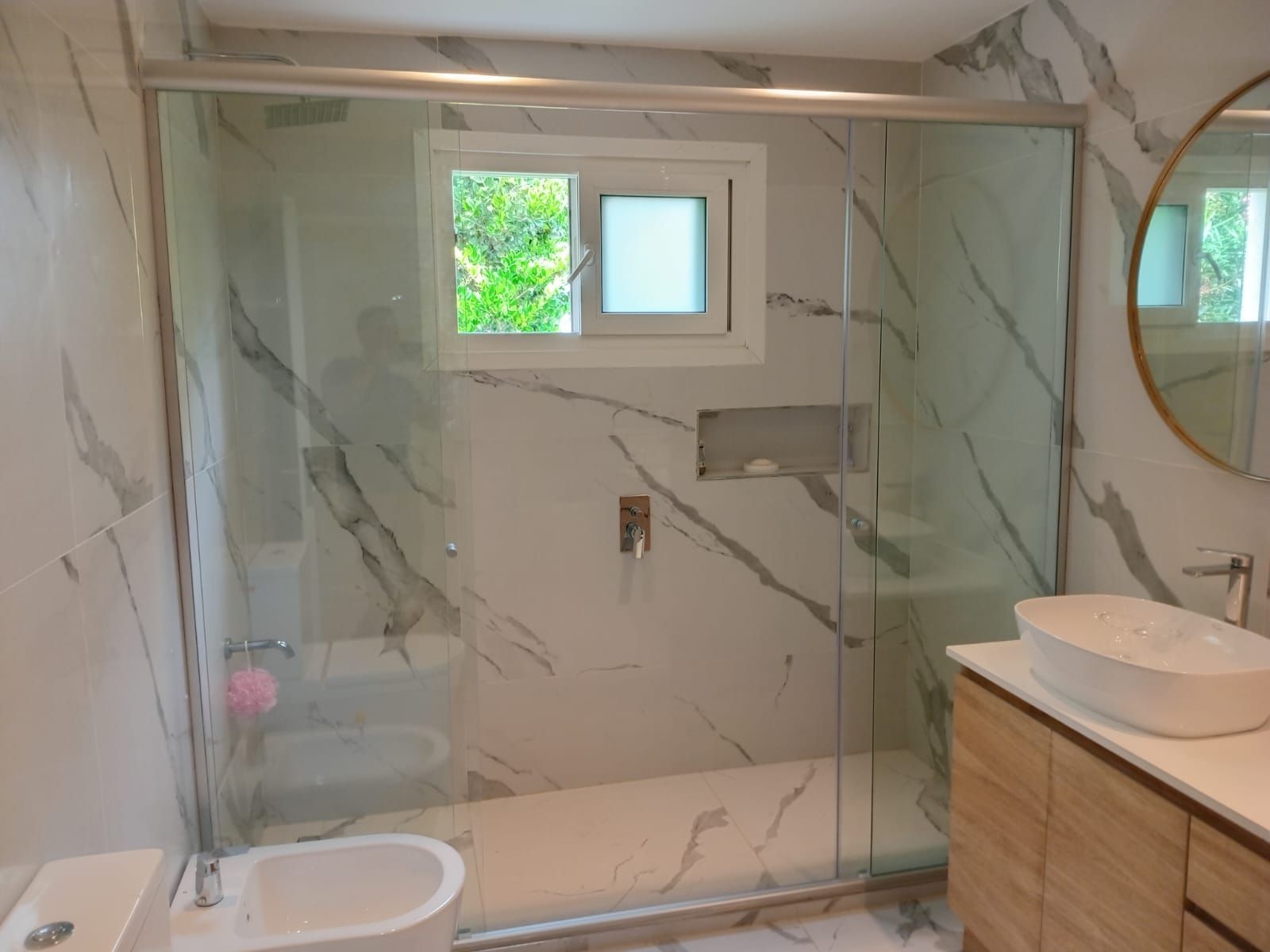 Baño moderno con paredes de mármol, ducha de cristal y tocador de madera.