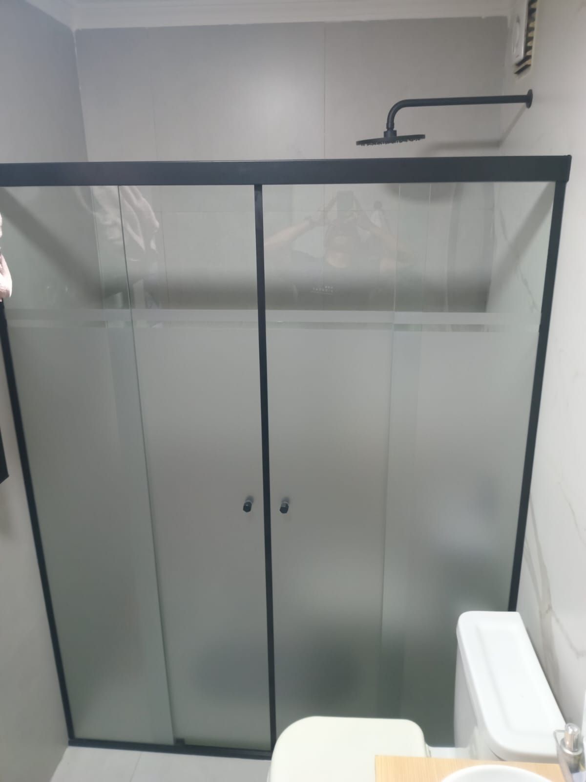 Cabina de ducha con marco negro y puertas de vidrio esmerilado, inodoro visible.