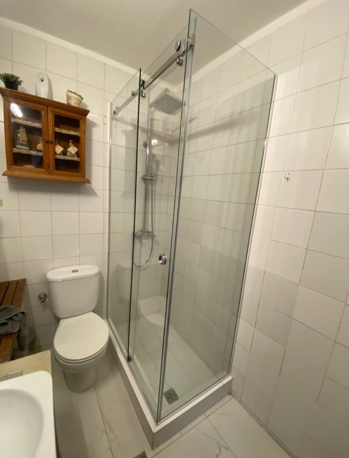 Baño con paredes de azulejos blancos, mampara de ducha de cristal y WC.