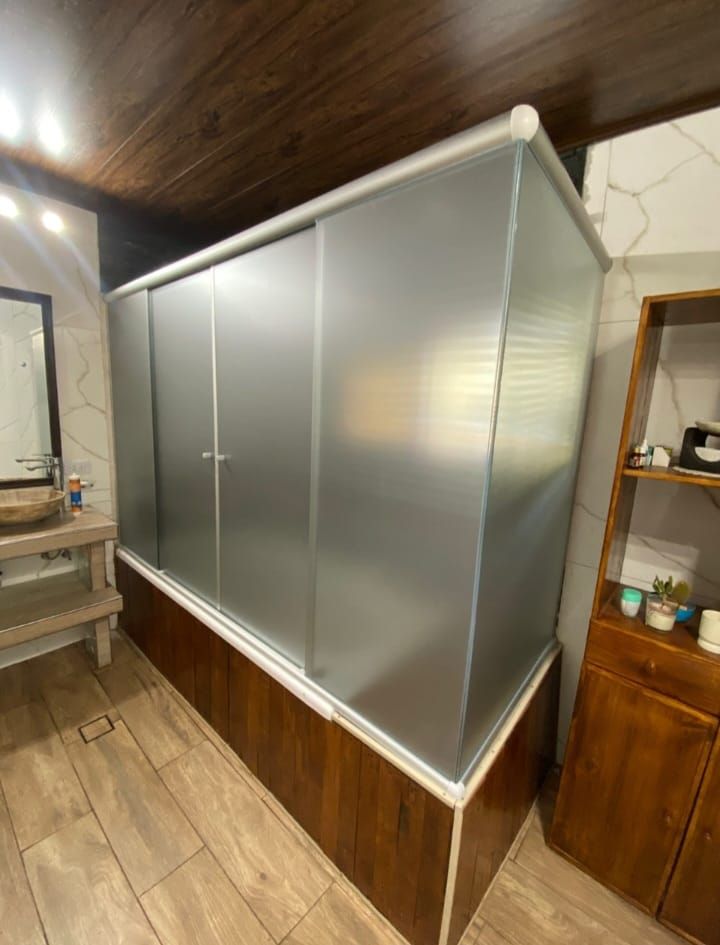 Cabina de ducha con puertas de vidrio esmerilado y detalles de madera en un baño.