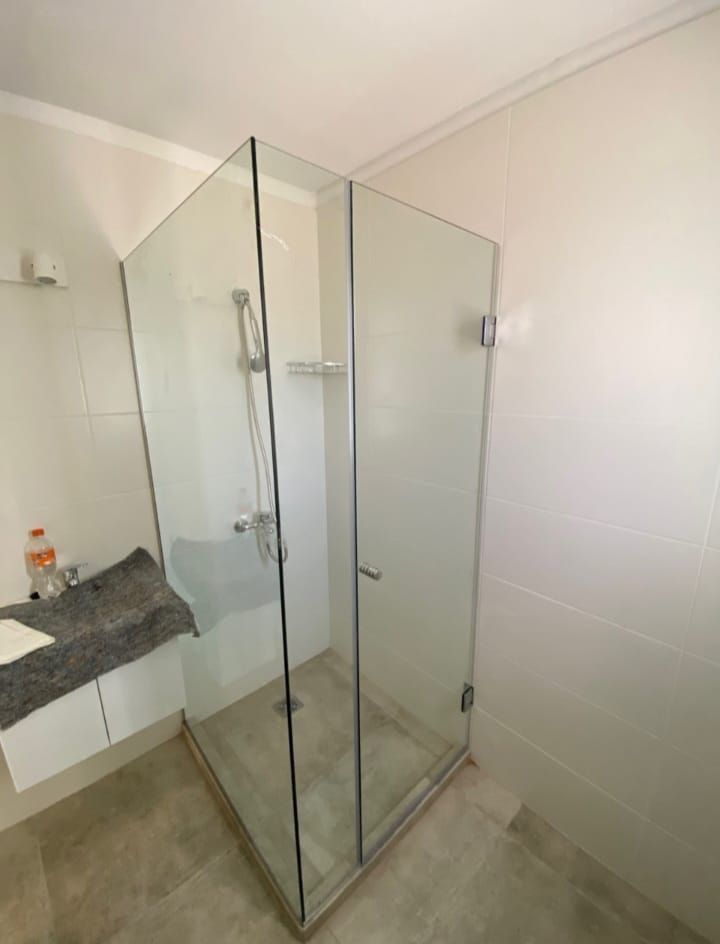 Mampara de ducha de cristal en baño con pared blanca y suelo gris.