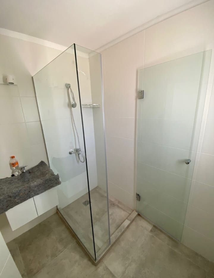 Ducha moderna de cristal con puerta esmerilada, cabezal de ducha y un pequeño lavabo incorporado en un baño de color claro.