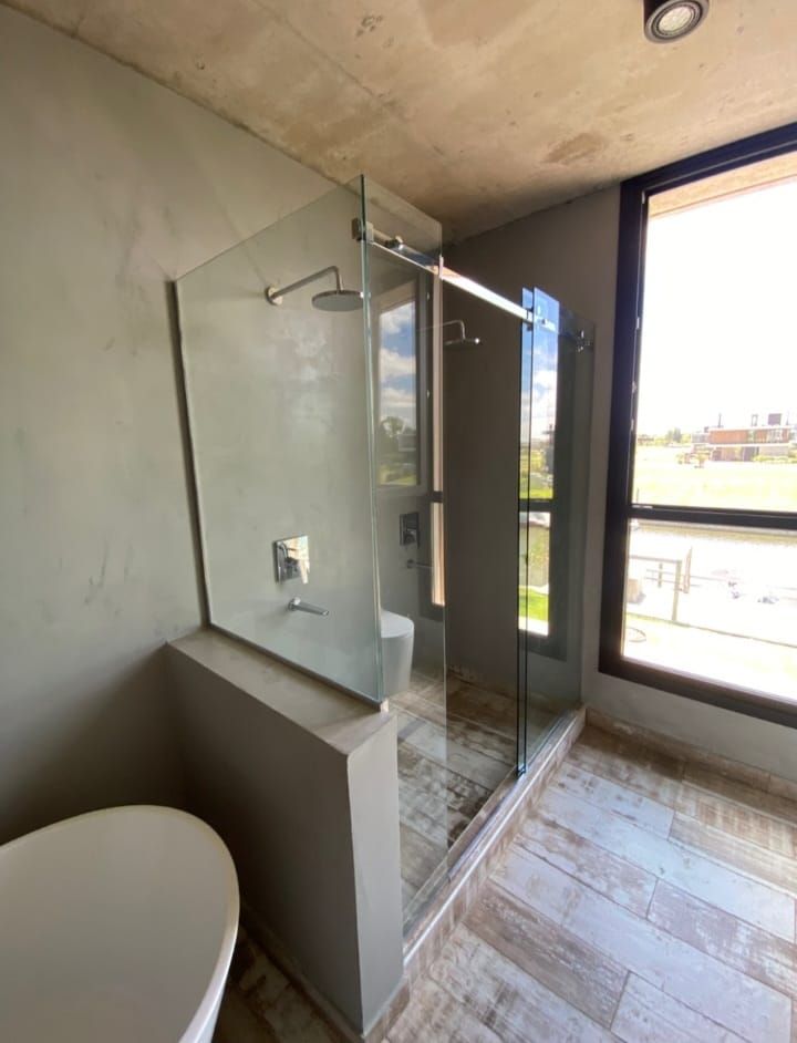 Ducha sobre bañera rodeada de mampara de cristal transparente y paredes de azulejos de color beige.