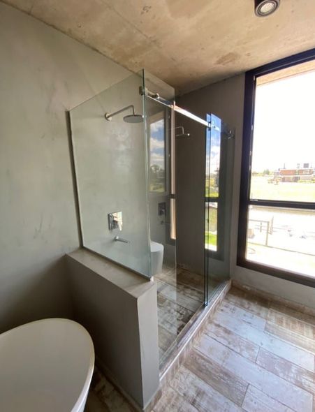 Ducha sobre bañera rodeada de mampara de cristal transparente y paredes de azulejos de color beige.