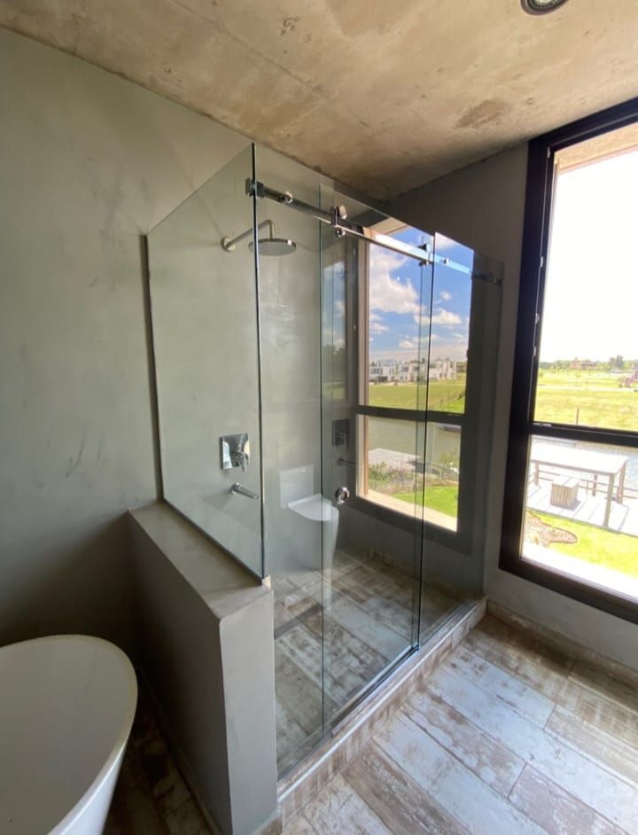 Moderna mampara de ducha de cristal con accesorios cromados junto a una ventana con vistas a un paisaje verde.