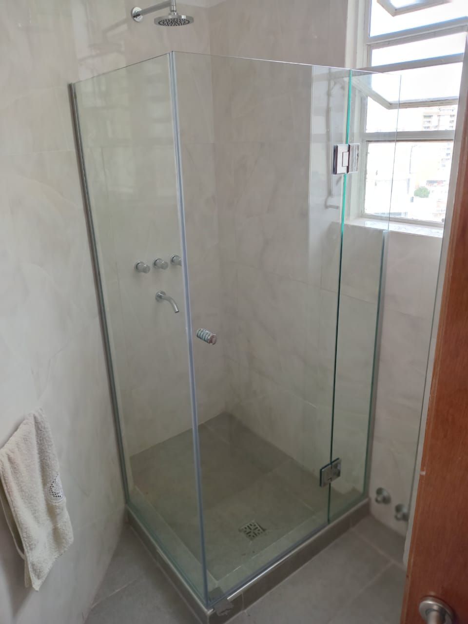 Mampara de ducha de cristal en baño con grifería plateada y ventana.