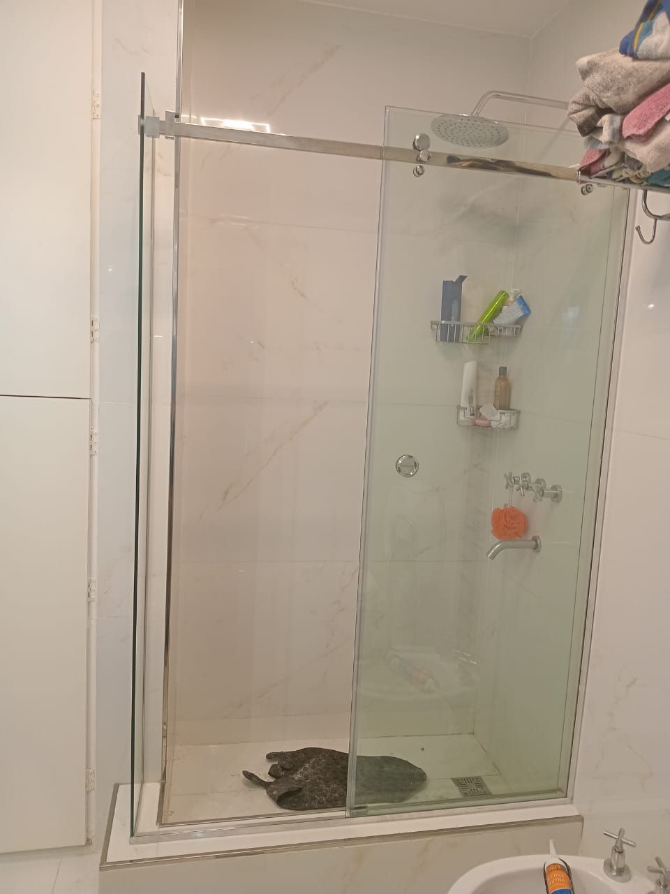 Cabina de ducha con puertas de cristal, jaboneras y toallero.