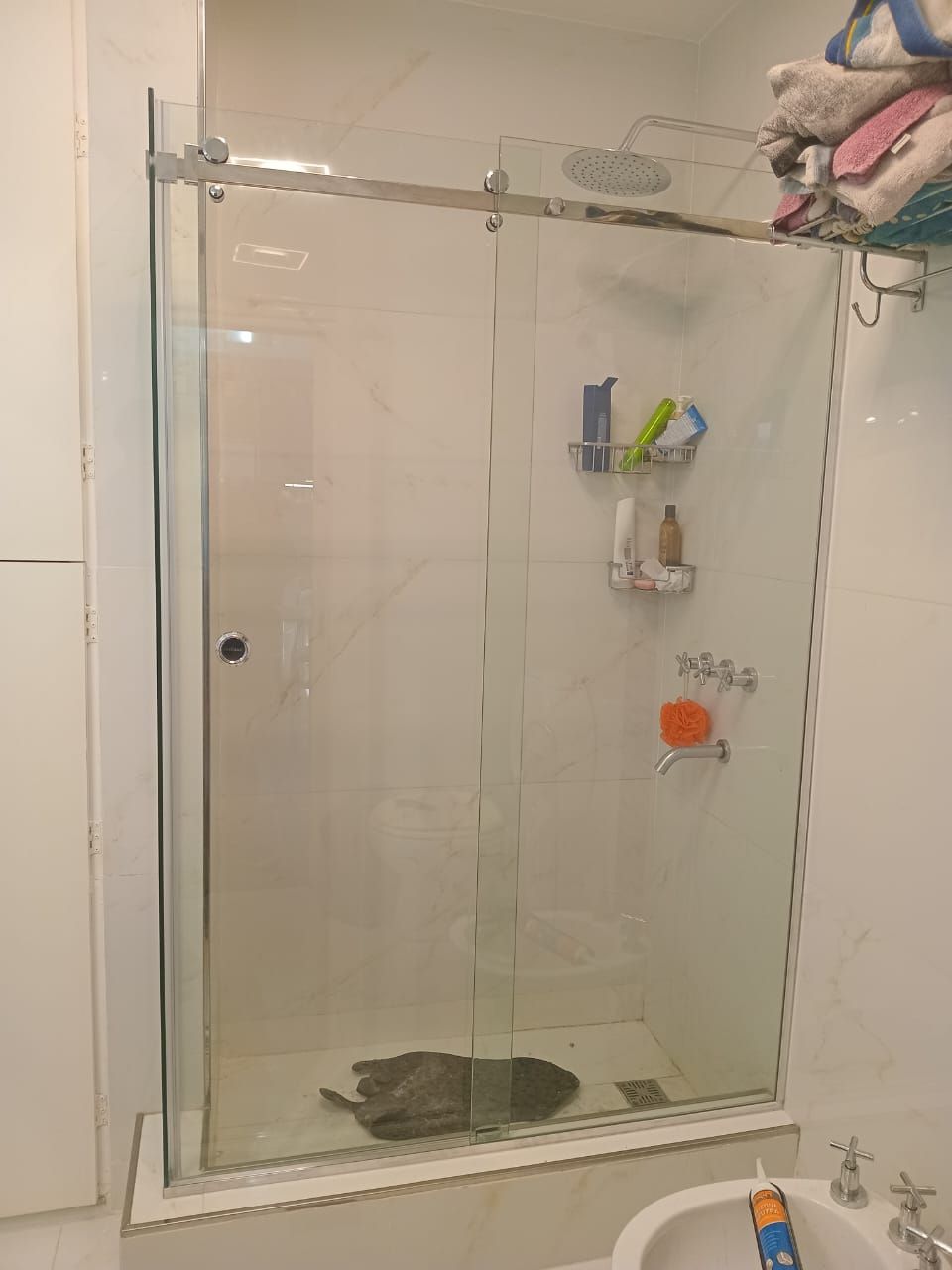 Mampara de ducha de cristal en baño con azulejos blancos.