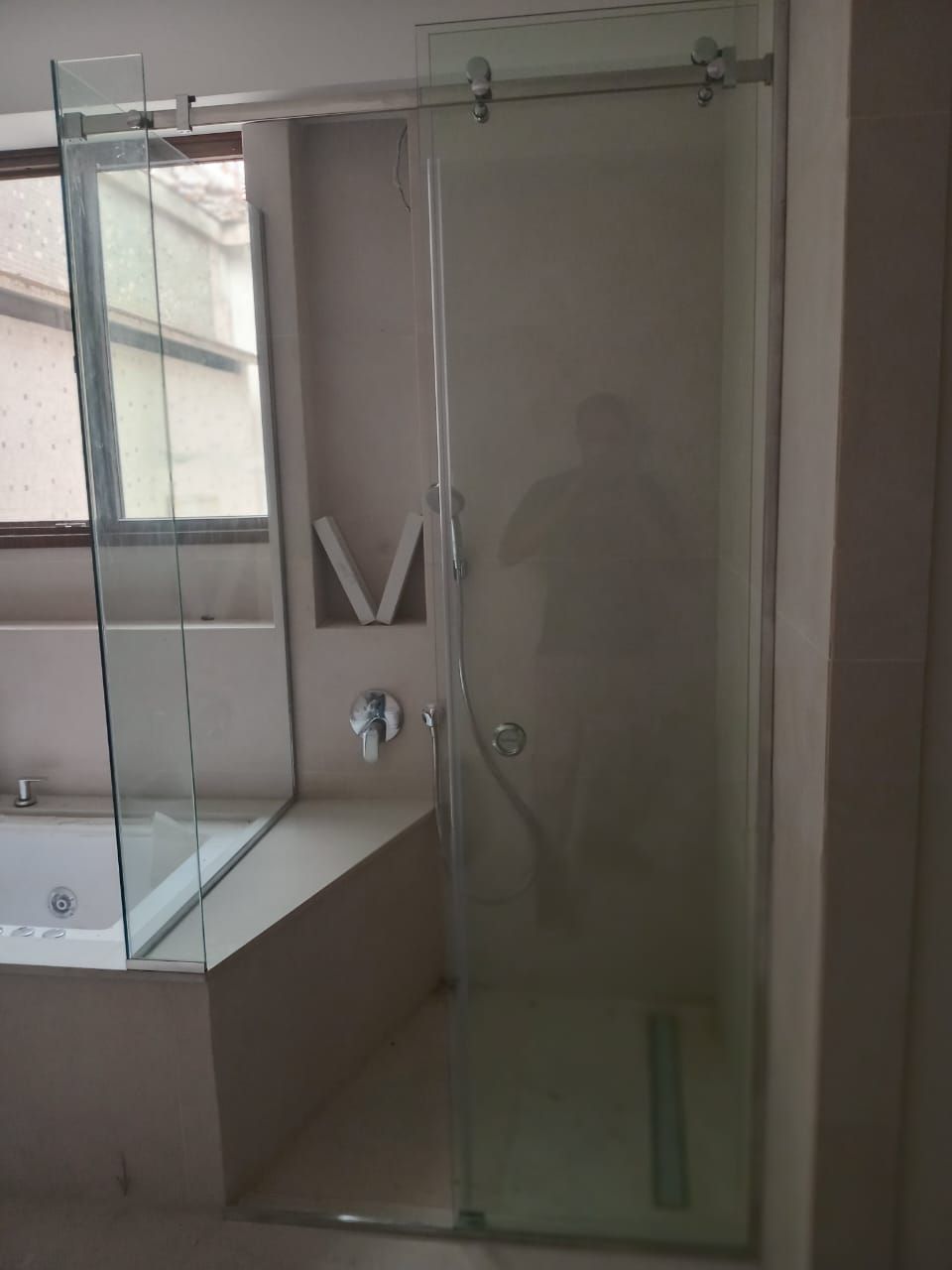 Mampara de ducha de cristal con puerta corredera junto a la bañera. La ducha tiene un rociador de lluvia.
