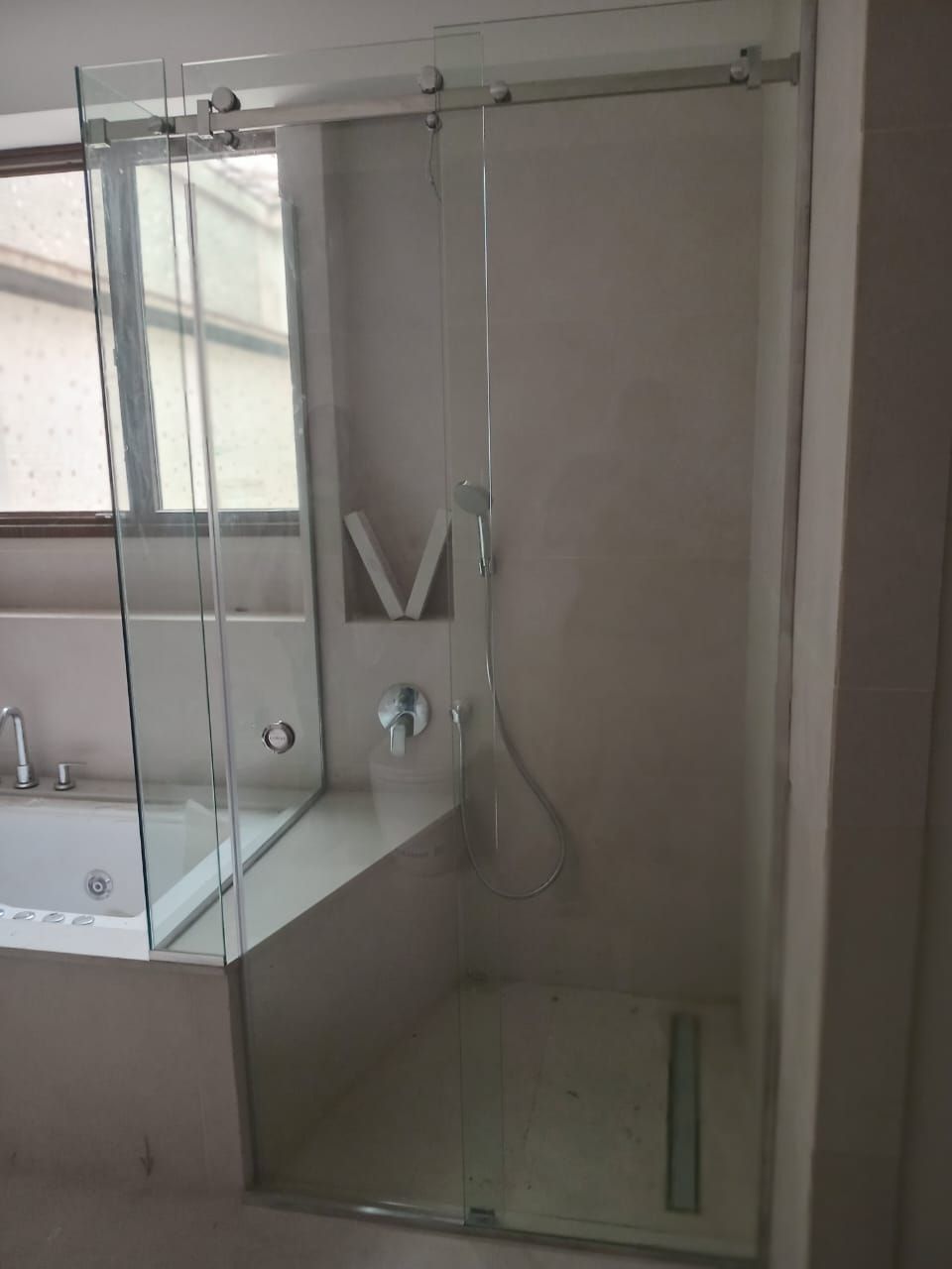 Mampara de ducha de cristal con puerta corredera junto a ventana y bañera.