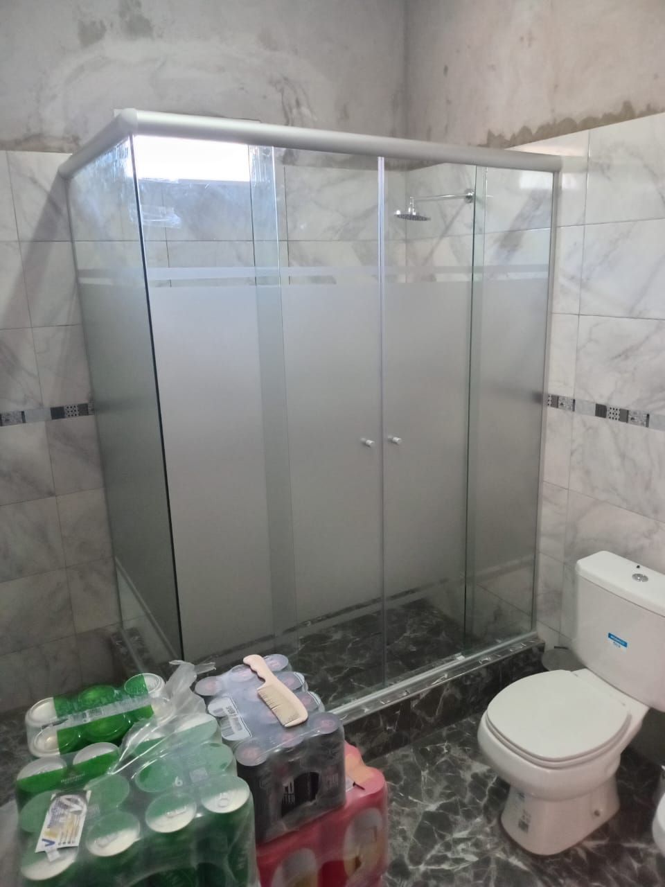 Mampara de ducha con paneles de cristal esmerilado, junto a inodoro, baño sin terminar.