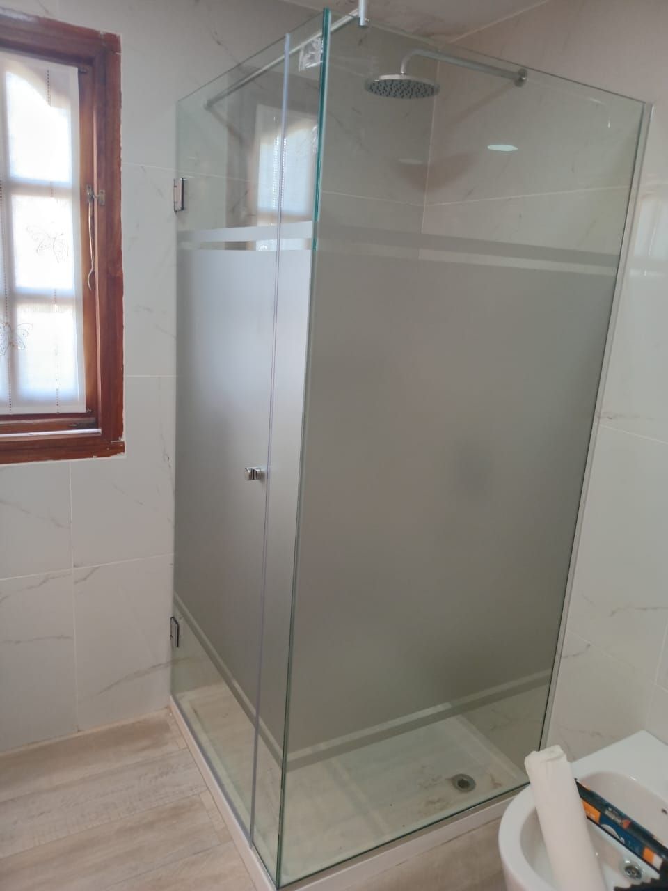 Mampara de ducha de cristal con puerta de cristal esmerilado y rociador de lluvia. Paredes blancas 