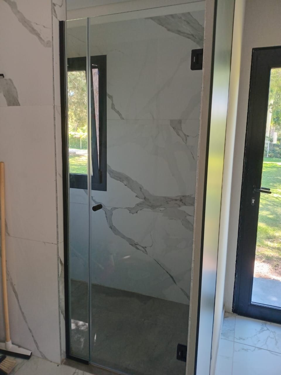 Puerta de ducha de cristal con marco negro en un baño con azulejos tipo mármol blanco.